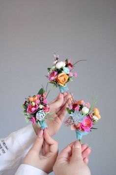 three hands holding small bouquets of flowers in front of a gray wall with writing on it