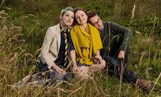 three people sitting in tall grass posing for the camera with their arms around each other