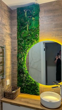 a person taking a photo of a bathroom with a mirror and plants on the wall