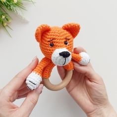 a hand holding a small crocheted orange teddy bear on a wooden toy ring