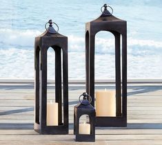 two black lanterns sitting on top of a wooden deck next to the ocean with lit candles