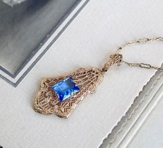 "Circa 1920 a lovely filigree lavaliere necklace crafted in 10k yellow gold set with a glittering cornflower-blue crystal gem. There's an amazing degree of intricacy to the airy design of the pendant with its graceful zig-zags and delicate milgraining, the glowing color of the metal perfectly complemented by the cool sparkle of the stone. Measuring approximately 1 1/2\" north to south including the decorative bail, and 3/4\" east to west. Hung on a fine 14k gold 15 1/8\" vintage crimp link chain Yellow Gold Filigree Jewelry For Evening, Heirloom Blue Necklaces For Weddings, Engraved 14k Gold Jewelry For Evening, Blue Art Deco Necklace For Formal Occasions, Fine Jewelry Filigree For Evening, Fine Jewelry With Filigree For Evening, Fine Jewelry For Evening With Filigree, Vintage Oval Diamond Cut Necklace, Evening Fine Jewelry With Filigree