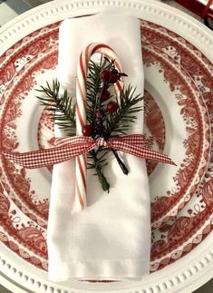 a christmas place setting with candy canes and greenery wrapped in red ribbon on a white plate