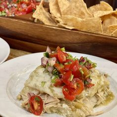 a white plate topped with tortilla covered in meat and veggies next to chips