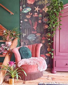 a pink chair sitting in front of a green wall with plants and other decorations on it