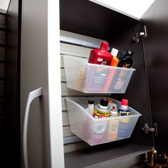 two plastic containers are on top of the shelf in this kitchen cabinet, and one is filled with cleaning products