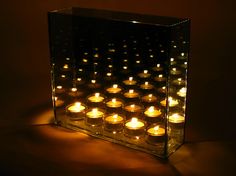 many lit candles in a glass block on a dark surface with light coming from the top