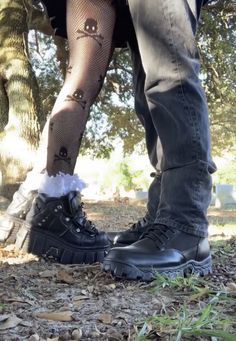 a man and woman standing next to each other under a tree wearing black boots with skulls on them