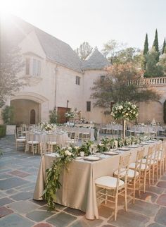 a long table with white flowers and greenery is set up in front of a large building