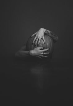 a black and white photo of two hands reaching out from behind a pumpkin in the dark