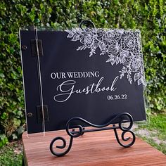 a black and white wedding guest book on a wooden table in front of some bushes