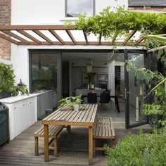 a wooden table sitting under a pergolated roof next to a kitchen and dining area