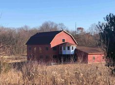 an old red barn sits in the middle of a field