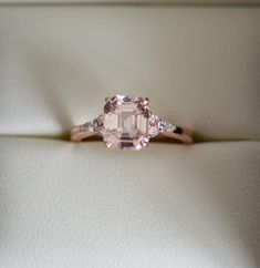 an engagement ring with a pink diamond and two white diamonds on the band, in a box