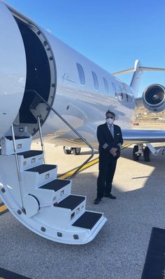 a man in a suit and tie standing next to an airplane stairs that lead up to the plane