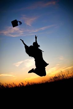 two people are jumping in the air with a book flying above their heads at sunset