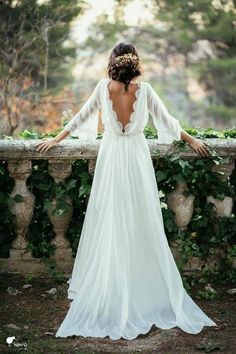 the back of a woman's wedding dress, with her arms on a stone wall