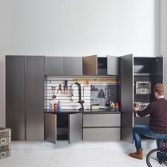 a man sitting on a bike in front of a kitchen with cabinets and tools hanging from the wall