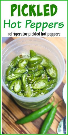 pickled hot peppers in a glass bowl on top of a wooden table next to green peppers