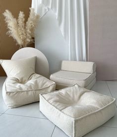 three different types of pillows sitting on the floor in front of a wall with white curtains