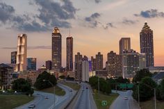 the city skyline is lit up at dusk with cars driving on the road in front of it