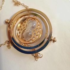 a gold and blue necklace with a clock on it's side, sitting on a white surface