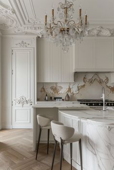 an elegant kitchen with marble counter tops and white cabinets, chandelier above the island