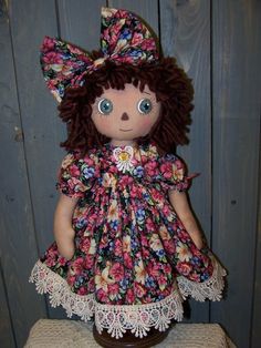 a small doll with brown hair and blue eyes wearing a floral dress on a stool