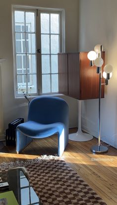 a blue chair sitting on top of a hard wood floor next to a lamp and window