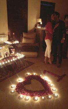 a man and woman standing in front of a heart shaped cake with candles on it