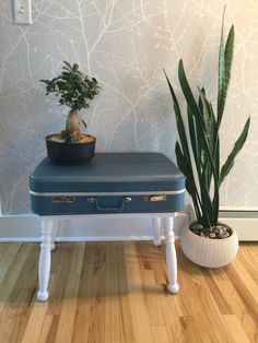 a blue suitcase sitting on top of a wooden table next to a potted plant