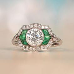 a diamond and emerald engagement ring with an oval center surrounded by smaller round brilliant cut diamonds