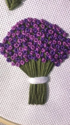 two purple flowers on a white surface with green stems in the middle, and one is made out of yarn