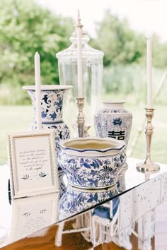 a table topped with blue and white vases on top of a wooden table next to candles