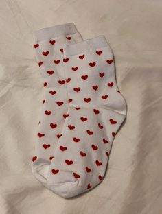 a pair of white socks with red hearts on them sitting on top of a bed