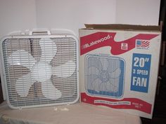 a white fan sitting on top of a table next to a cardboard box with it's lid open