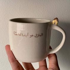 a hand holding a white coffee cup with writing on the side and a piece of bread sticking out of it