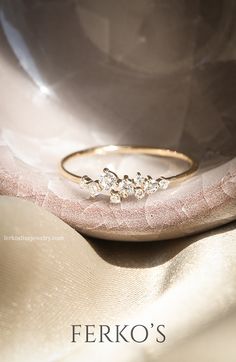 a gold ring with three small diamonds on it sitting on top of a pink cloth