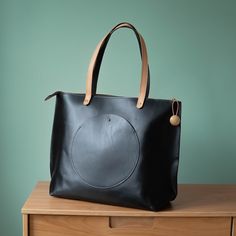 Made from a full grain, oil tanned leather in black. Oil tan leathers are very durable, water resistant, and only get better with age. Measures 19" w x 14"h x 6"d. Great for weekend travel, as a diaper bag, or a large work tote. Strap drop length measures 13" Features a round exterior pocket, a round interior pocket, and a handy pen pocket. Designed and handmade in our Richmond, Virginia studio. Modern Canvas Tote Bag With Leather Trim, Modern Tote Shoulder Bag With Brass Hardware, Leather Tote Bag With Brass Hardware, Leather Tote Bag With Hardware Details, Sleek Textured Leather Tote Bag, Tanning Oil, Work Tote, Weekender Tote, Solid Metal