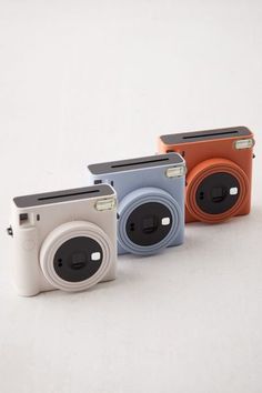 three different colored cameras sitting next to each other on a white surface with one camera facing the viewer