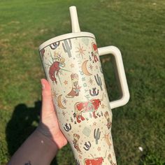 a person holding up a cup with animals on it in the middle of a field