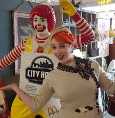 a woman standing in front of two large ronald mcdonald's characters, one holding a sign