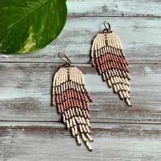 the beaded earrings are hanging from hooks on a wooden table next to a green leaf