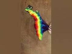 a rainbow colored kite laying on top of a wooden floor next to a person's hand