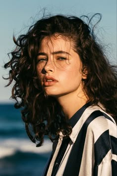 a woman with curly hair standing in front of the ocean