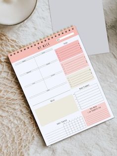 a pink and white planner sitting on top of a table next to a cup of coffee