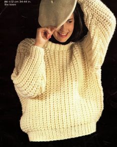 a woman in a white sweater and hat posing for the camera with her hands on her head