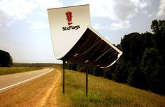 an upside down billboard sitting on the side of a road next to a lush green field