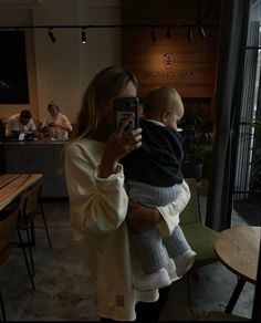 a woman holding a baby taking a selfie with her cell phone in front of her