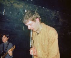 two young men are singing into microphones in a dark room while another man is playing the guitar